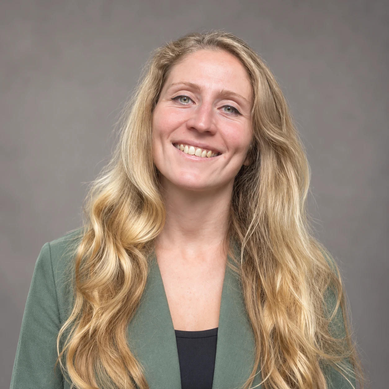Portrait of Fruzsina Funtek smiling, with long wavy blonde hair, wearing a green blazer